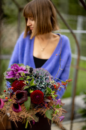 Portrait of a young woman standing with beautiful bouquet of flowers in glasshouse in gardenの写真素材