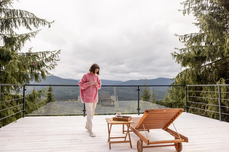 Woman in pink sweater rests with her dog on a spacious white terrace in mountains. Recreation in house on nature conceptの写真素材