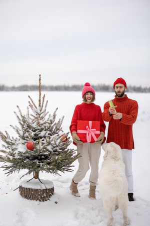Man and woman have fun together, shooting confetti near Christmas tree outdoors. Young couple celebrating New Years holidays togetherの写真素材