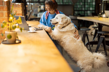 Woman sits with her cute adorable dog at modern coffee shop and works on laptop. Pet friendly places...