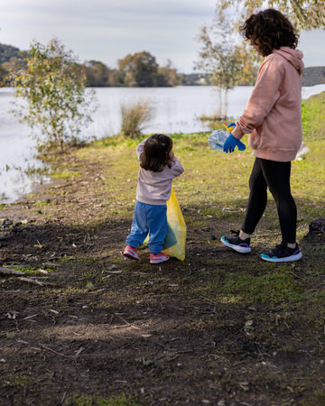 Single-parent family of a mother and daughter clearing the countryside of plastic waste on a...