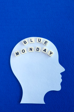 This minimalist image features a white silhouette of a human head, with the words "Blue Monday" placed inside the head using letter tiles. The entire composition is set against a vivid blue background, symbolizing the concept of depression, mental health, and the "Blue Monday" phenomenon, which refers to the most depressing day of the year.の写真素材
