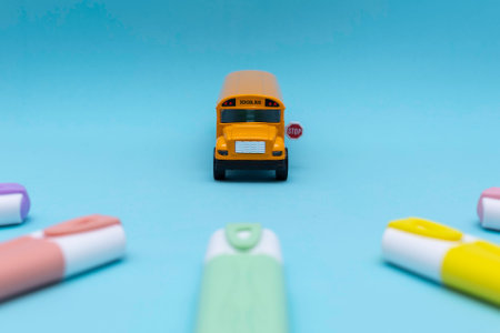 Toy yellow school bus seen from the front with a visible stop sign, surrounded by colorful markers on a solid blue background. The setup evokes themes of education, school transportation, and childhoodの写真素材