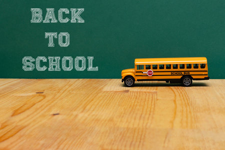 A yellow toy school bus is placed on a wooden table in front of a green chalkboard with the phrase âBack to Schoolâ written in white letters, representing the beginning of the academic yearの写真素材
