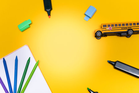 School supplies including crayons, colored pencils, markers, notebook and a yellow toy school bus...