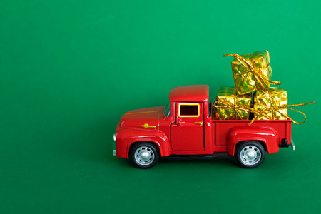 A red toy truck carrying gift boxes wrapped in gold paper, for Christmas, on a green backgroundの写真素材