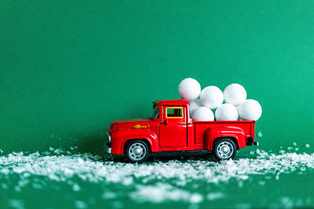 Colorful holiday-themed image of a red toy pickup truck loaded with white snowballs, placed on...