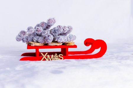 Decorative red sleigh on snow, loaded with frost-covered branches and resting on small wooden logs. On the side, there is a gold detail with the word âXMASâの写真素材