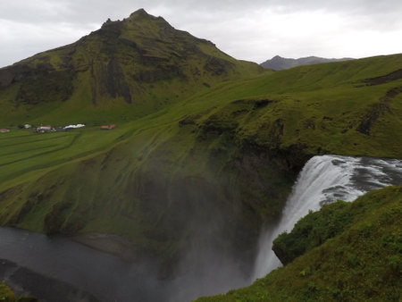 Scenic view of a waterfall and a green meadow under a gray sky in Icelandの写真素材