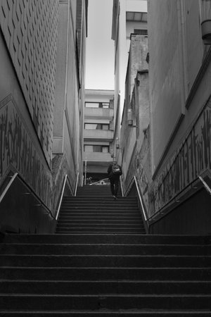 Grayscale shot of a man climbing stairs between buildingsの写真素材