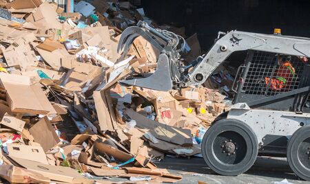 Victoria, British Columbia / Canada- 30/04/2019: A bobcat operator piles waste cardboard for processing at a commercial recycling facility.のeditorial素材