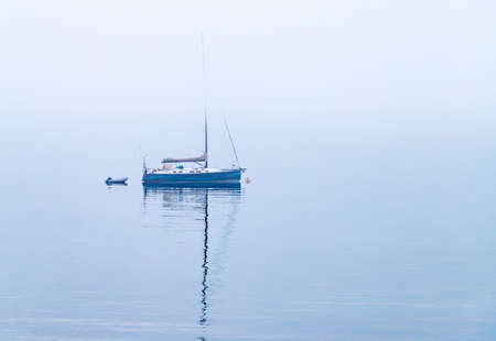 A lonely sailboat sits in fog covered water.の写真素材