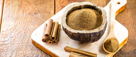 powdered cinnamon in a rustic bowl, with pieces of cinnamon in the shell around, a culinary spice in...