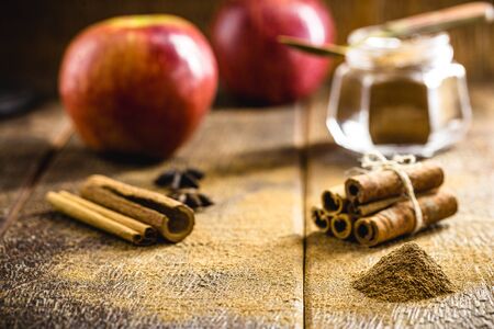 Ground cinnamon, cinnamon sticks, with apples in the background, wooden background in a rustic style. Spot focus.の写真素材