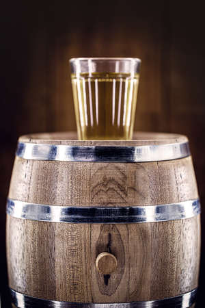 aged oak barrel with glass of distilled beverage used for fermented drinks such as rum, cachaÃ§a, vodka, among others. Spot focus on the barrel.の写真素材