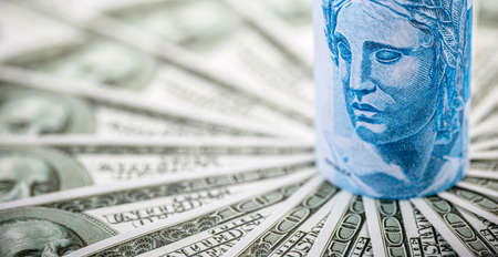 high dollar, devaluation of the real, 100 Brazilian reais banknote among many hundred dollar bills, concept of financial crisis brazilの写真素材