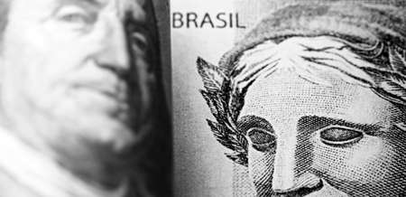 detail of a banknote of 100 reais from brazil beside a hundred dollar bill of american dollars, gloomy scenario, crisis, economic devaluation, punctual focusの写真素材
