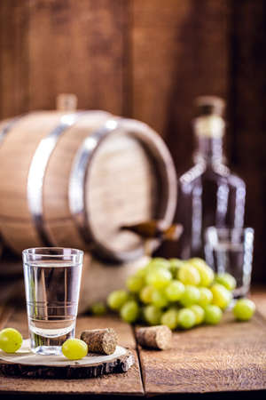 Glass of brandy based on grapes, called bagaceira in Portugal and in Italy Grappa or Graspa, with oak barrel in the backgroundの写真素材