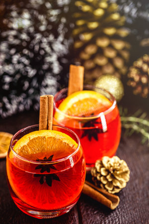 Mulled red wine with spices and Christmas fruits on a rustic wooden table with Christmas colors and lights. Traditional hot drink at Christmas timeの写真素材