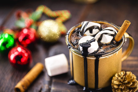 chocolate and hot cocoa with marshmallow in a golden ceramic mug surrounded by christmas things on a rustic wooden table. The concept of cozy holidays and New Year and Christmas.の写真素材
