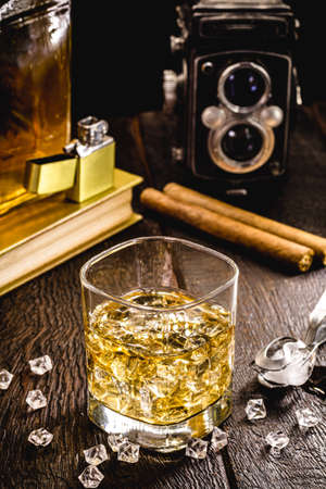 whiskey with ice on a wooden table, with decorative objects in the background, cigar, lighter and book.の写真素材