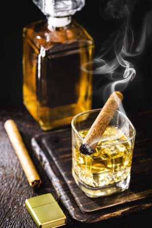 whiskey or bourbon, distilled drink with malt in a glass with ice cubes, with a lighted cigar on the side, soft smoke. Time to relax, lifestyleの写真素材