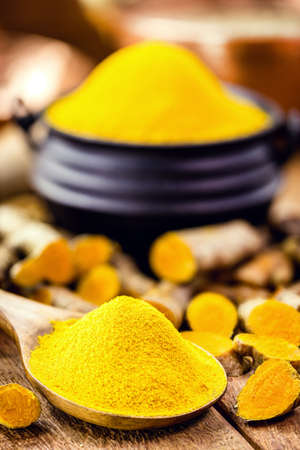 spoonful of turmeric powder, turmeric roots in a wooden bowlの写真素材