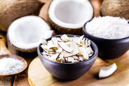 coconut chips, shavings and pieces of coconut inside a clay bowl, with many ripe coconuts in the...