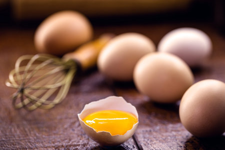 broken country chicken egg, visible yolk on wooden table, cooking with organic eggsの写真素材