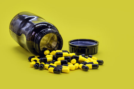 bottle of black and yellow pills on yellow background, caseia aor caffeine pills used in bodybuilding for muscle massの写真素材