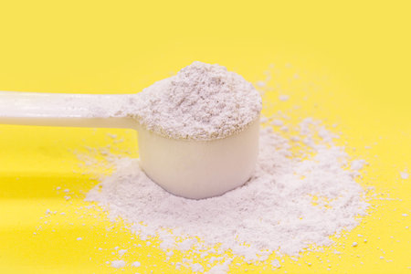 measuring spoon with casein or caffeine powder, food supplement, vitamin used by athletes, yellow backgroundの写真素材