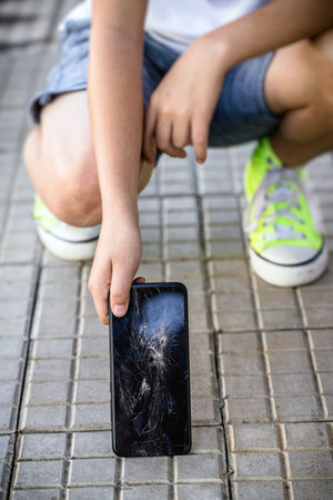 child picking up broken smartphone from the floor, broken cell phone screen, cracked protective filmの写真素材
