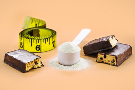 measuring spoon of creatine or casein doses and protein chocolate bars next to tape measure, copyspace, dietary supplement conceptの写真素材
