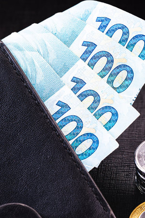 wallet full of money from Brazil, one thousand reais on one hundred reais bank notes. With coins in the background. Financial savings concept.の写真素材