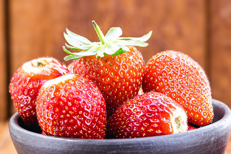 handmade clay pot with Brazilian strawberries of the Albion variety, wooden background, copyspaceの写真素材