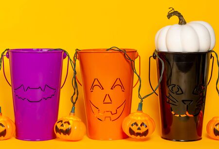 Purple, orange, and black decorative Halloween buckets with a white pumpkin and orange jack o lantern lights on an orange background with room for textの写真素材