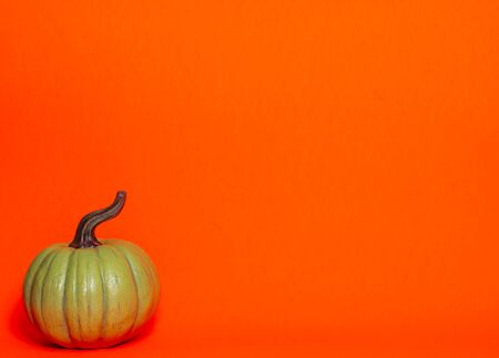 Green decorative thanksgiving pumpkin front view on an orange background with room for textの写真素材
