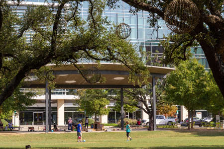 green open space in a park with a modern blue glass building in the background and people walking in the distanceのeditorial素材
