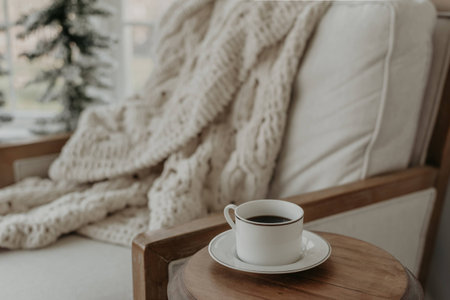 Cup of coffee with cable knit blanket on chair in living roomの写真素材