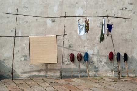 Mops and Laundry 2 - Wuzhen, China. Laundry, mops and mat. Wooden pole rack holding laundry and a mat. Mops against a stucco wall. Wuzhen, China.のeditorial素材