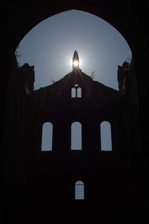 Plants grow atop the stone walls of this ruined cathedral, and sun flare enhances religious feeling of this ruined cathedral. Old windows silhouettedの写真素材