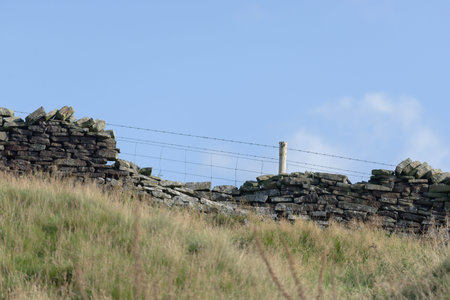 Profile of drystone wall and barbed wire fence against pastel blue sky background. Autumn rural season in the peak district, selective focus texture.の写真素材