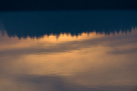 A warm orange glowing sunset behind a line of conifer trees is reflected and displayed upside down...