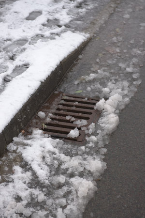7 - Urban highway drain covered in thawing snow fall. Water runs along the curbside and into the surface storm drain. This area is at risk of floodingの写真素材