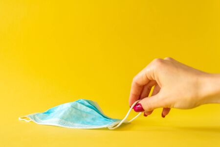 Procedure mask. Woman hand taking a surgical mask with rubber ear straps on yellow background. selective focus. Protection conceptの写真素材