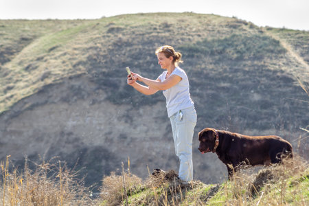 woman taking photo to smartphone standing with a dog Labrador retriever.