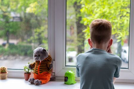 Young boy looking at window. He is sad and unhappy. Self isolation, stay at home during pandemic of covid-19の写真素材