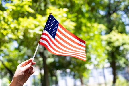 Happy Independence Day of USA. American Flag in women hand on green tree background. Fourth of Julyの写真素材
