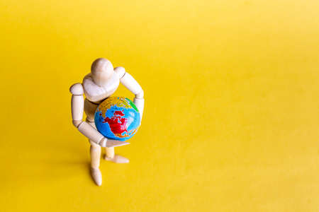 Wooden mannequin holding globe in hands on yellow backgroundの写真素材