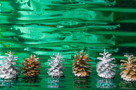 Metallic silver and gold pine cones at shiny green background. Copy spaceの写真素材
